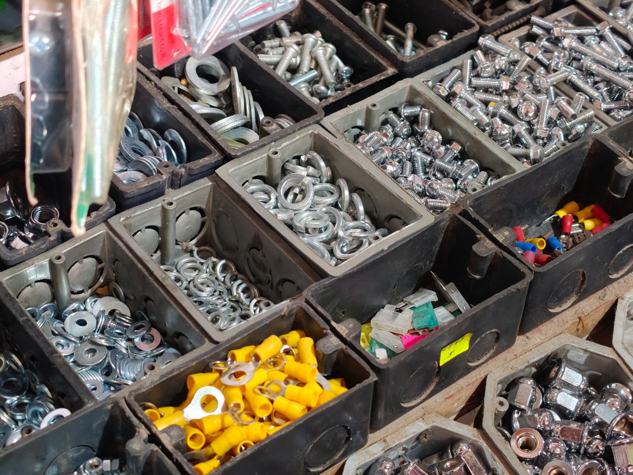 Close-up view of various hardware fasteners in black storage bins, including nuts, bolts, and washers.